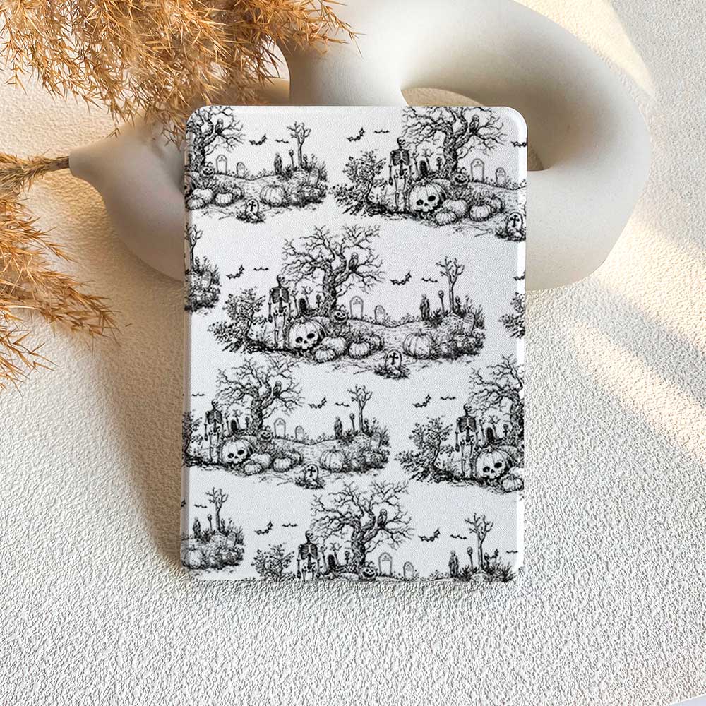 A black Kindle case with a vintage Halloween pattern featuring skulls and trees, displayed on a white background with a decorative vase in the background.