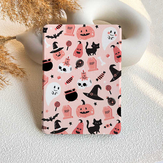 A pink Kindle case with a pattern of Halloween-themed characters and motifs, including ghosts, pumpkins, and cats, displayed on a table with a decorative background.