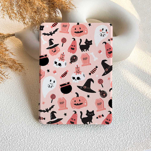 A pink Kindle case with a pattern of Halloween-themed characters and motifs, including ghosts, pumpkins, and cats, displayed on a table with a decorative background.