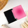 Two square folding color cards or swatches, one black and one bright pink, displayed on a white surface with decorative props including a woven fan and dried grass.
