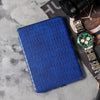 Blue crocodile-patterned case on a gray surface with a watch and camera.