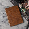 Brown textured wallet and green watch on a gray surface with 'Hugo' branding.
