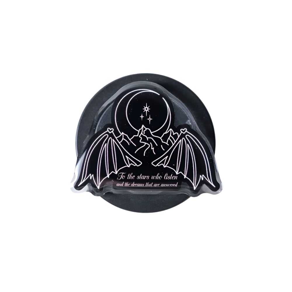 Black and white decorative item with bat wings and celestial design on a light gray background