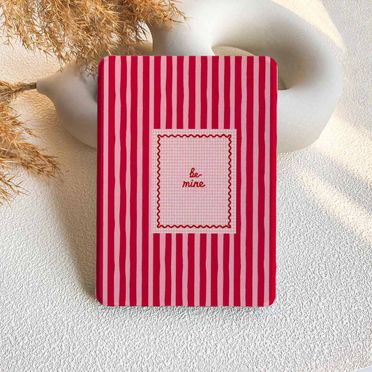 Red and white striped notebook with 'be mine' text on a textured surface