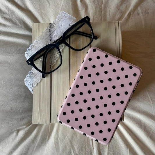 Pink case with black polka dots on a wooden surface with glasses and lace.