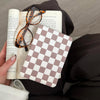 Person holding an open book with a checkered kindle case and tortoiseshell glasses on top.
