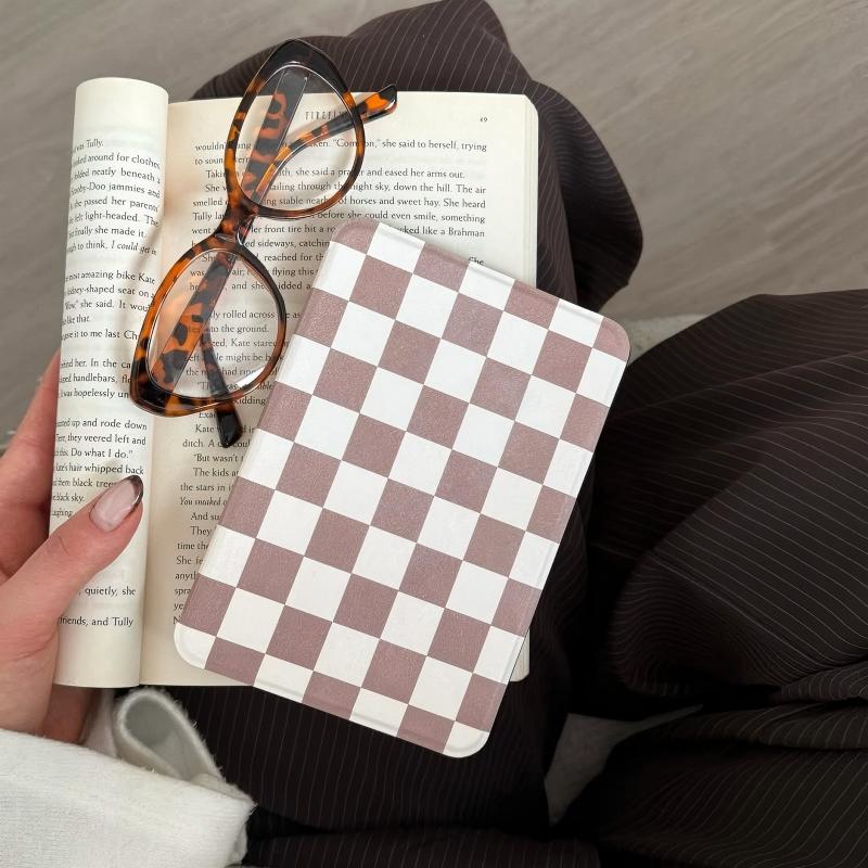 Person holding an open book with a checkered kindle case and tortoiseshell glasses on top.