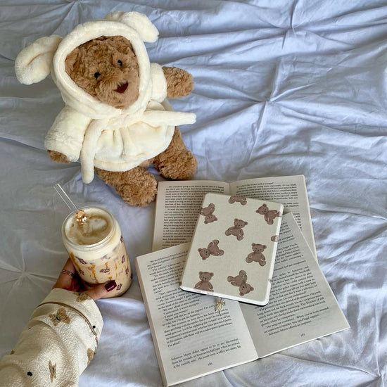 Teddy bear in a robe with a book and coffee on a white surface