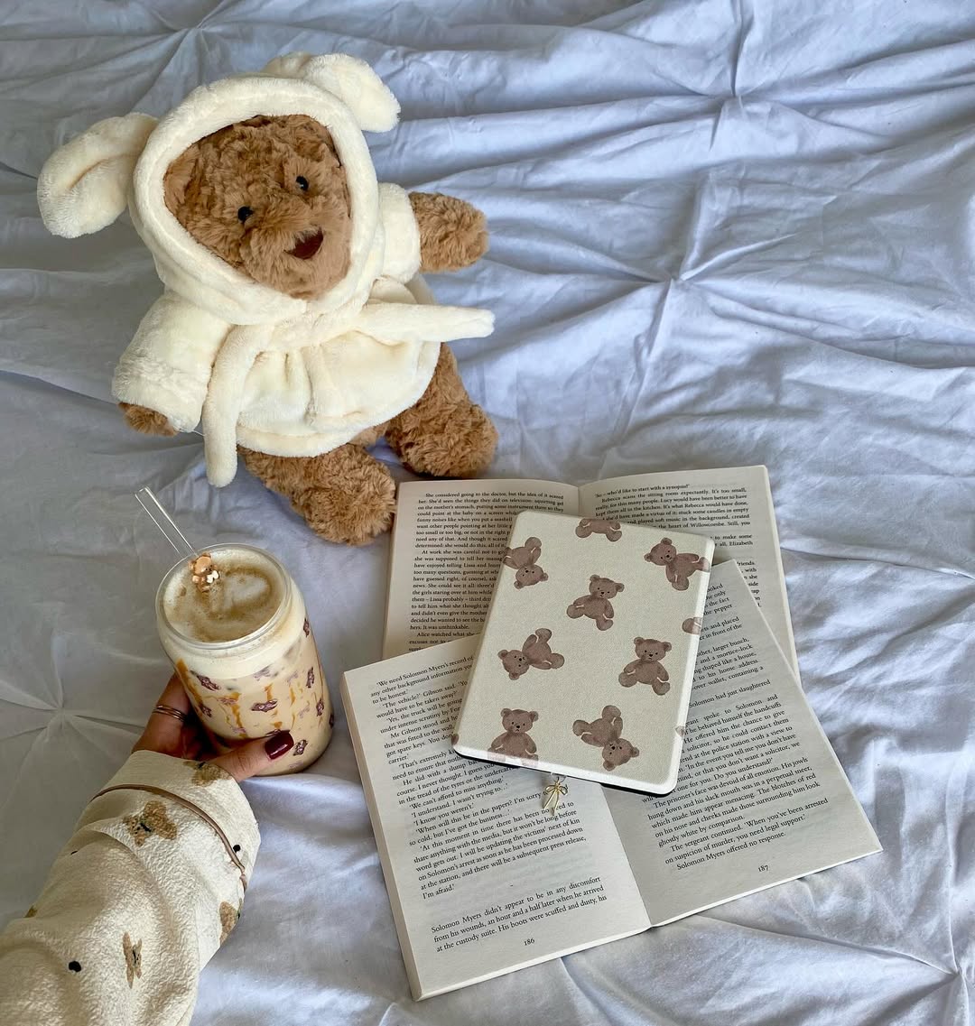 Teddy bear in a robe with a book and coffee on a white surface